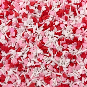 May include: A close-up image of a variety of red, pink, and white heart-shaped sprinkles and white sprinkles. The sprinkles are perfect for decorating cakes, cupcakes, cookies, and other desserts.