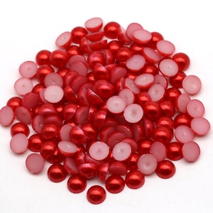 May include: A pile of red pearl-like beads with a white interior. The beads are round and have a glossy finish.