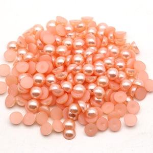 May include: A large pile of peach-colored pearl-like round beads. The beads are flat on one side and have a rounded dome on the other side.