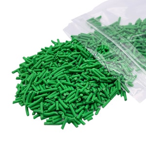 May include: A close-up of a bag of green sprinkles. The sprinkles are long and thin, and they are spilling out of the bag.