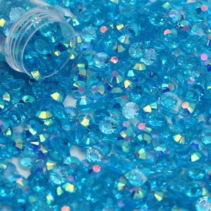 May include: A close-up image of a large quantity of small, round, turquoise blue rhinestones. The rhinestones have a faceted, iridescent finish, giving them a sparkly appearance.