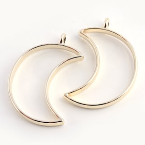 May include: Two gold metal crescent moon shaped pendant blanks. The blanks are open and ready to be filled with resin or other materials.