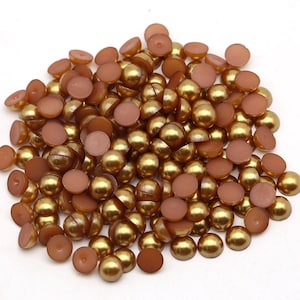 May include: A large pile of gold-colored half-round pearl beads. The beads have a smooth, shiny finish and are perfect for crafting projects.