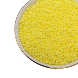 May include: A white bowl filled with bright yellow foam beads.