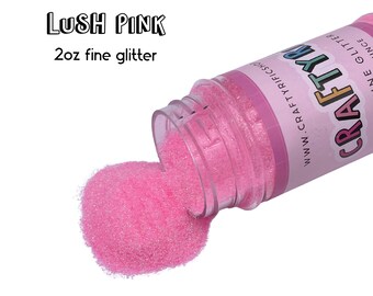 May include: A 2 oz bottle of Lush Pink fine glitter, spilling out onto a white background. The bottle is labeled "CRAFTY" with the website address "www.craftyrifics.com".