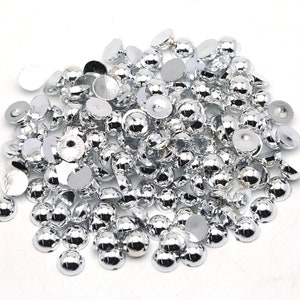 May include: A large pile of silver round flat-back cabochons. The cabochons are shiny and have a domed top.