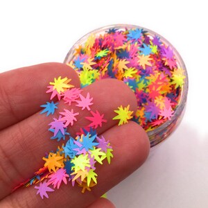 May include: A jar filled with colorful glitter shaped like maple leaves. The glitter is a mix of pink, yellow, blue, green, and orange.