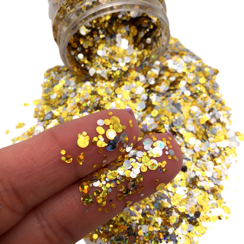 May include: A close-up of a pile of gold and silver glitter. The glitter is in the shape of small circles and is being held in a person's hand.