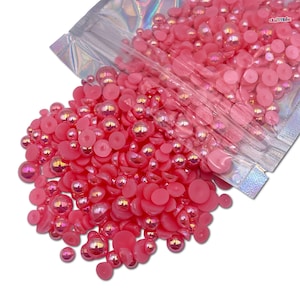 May include: A bag of pink pearl and flat back embellishments. The bag is open and the embellishments are spilling out.