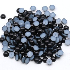 May include: A pile of black and light blue half-round cabochons. The cabochons are smooth and glossy, with a flat back. The light blue cabochons have a matte finish. These craft supplies are suitable for jewelry making and other DIY projects.