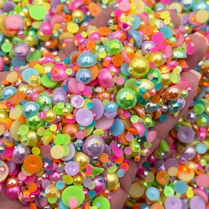 May include: A large assortment of colorful, iridescent, and opaque round and flat beads in various sizes. The beads are a mix of pastel and bright colors, including pink, blue, green, yellow, and orange.