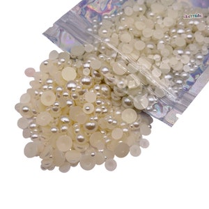 May include: A bag of white pearl-like beads and flat round embellishments. The bag is open and the beads are spilling out.