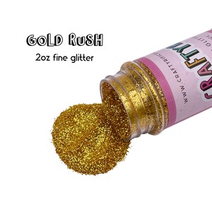 May include: A 2 oz jar of fine gold glitter, spilling out onto a white background. The jar is labeled "GOLD RUSH" and "CRAFTY" with the website address "www.craftyrecs.com".