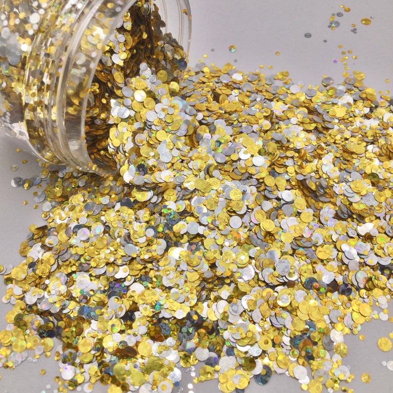 May include: A close-up of a jar of gold and silver glitter. The glitter is spilling out of the jar and is scattered on a white surface.