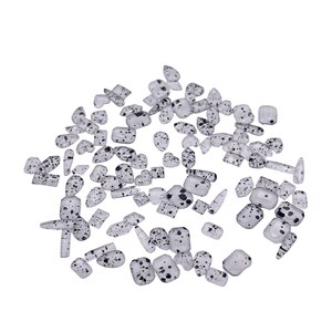 May include: A scattering of small, clear glass beads with black speckles. The beads are of various shapes and sizes, including round, oval, and rectangular.