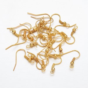 May include: A close-up of a pile of gold-toned earring hooks. The hooks are made of metal and have a spring-loaded closure.