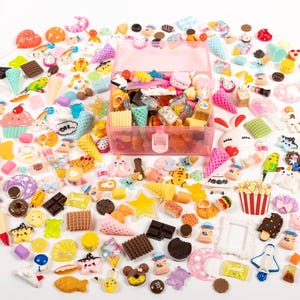 May include: A collection of colorful miniature food and dessert charms, including cupcakes, ice cream cones, and chocolate bars, spilling out from a pink storage box. Various shapes and sizes, with a white background.
