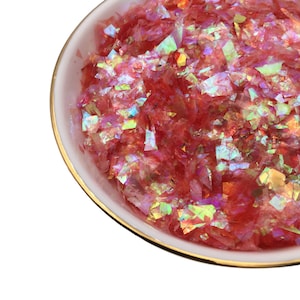 May include: A bowl filled with iridescent pink and gold glitter flakes. The glitter is perfect for adding sparkle to crafts, resin projects, and more.