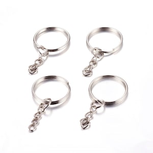May include: Four silver-colored keychains with split rings and chain links. The key rings are circular and have a small chain attached for keys or charms. The keychains are on a white background.