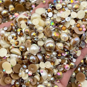 May include: A large assortment of pearl and iridescent brown and white beads. The beads are various sizes and shapes, including round, half-round, and flat.