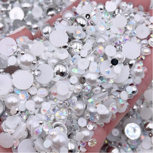 May include: A mix of white and silver pearl and rhinestone embellishments. The embellishments are various sizes and shapes, including round, oval, and teardrop.