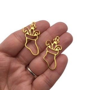May include: Two gold metal Christmas stocking charms with a decorative top. The charms are cut out and have a smooth, shiny finish.