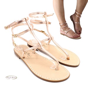 Puede incluir: Sandalias de cuero color oro rosa con múltiples correas y hebillas. Las sandalias tienen un dedo del pie en forma de tanga y una suela plana.