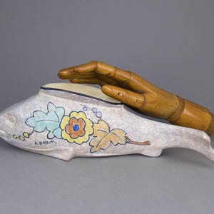 Könnte beinhalten: Eine Keramik-Fischschale mit einem Blumendesign in Blautönen, Grün, Gelb und Orange. Die Schale ist mit der Signatur "A. Dubuis" verziert und ruht auf einer Holzhand.