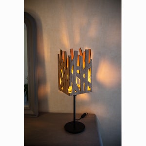May include: A modern table lamp with a wooden geometric shade and a black metal base. The shade is lit from within, casting a warm glow.