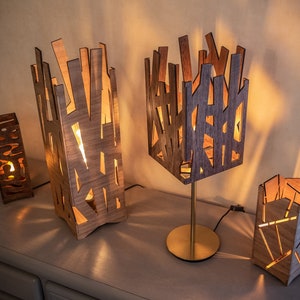 May include: Four wooden lamps with geometric designs, lit and casting warm light. The lamps are made of thin strips of wood, creating a unique and modern look.