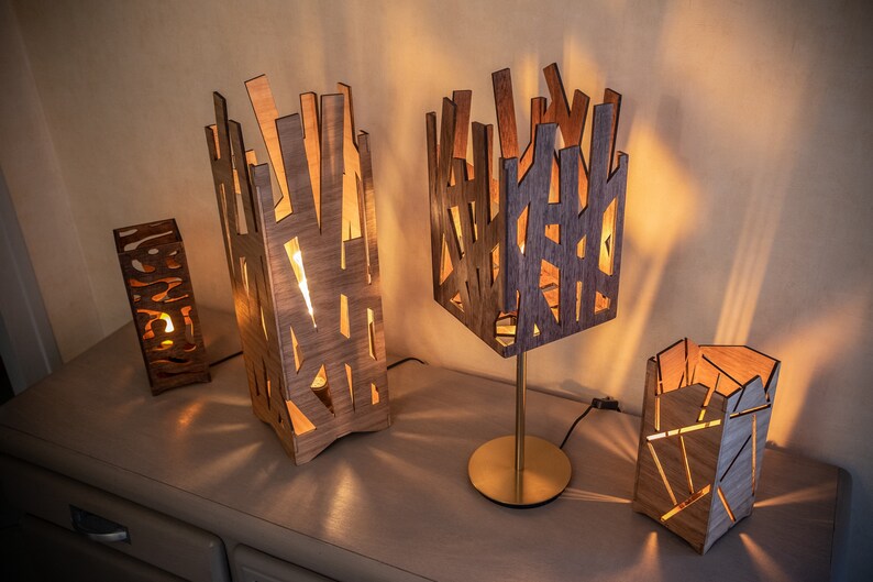 May include: Four wooden lamps with geometric designs, lit and casting warm light. The lamps are made of thin strips of wood, creating a unique and modern look.