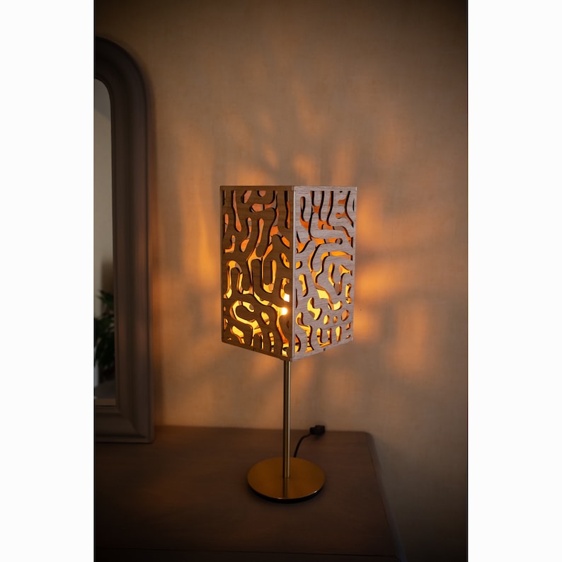 May include: A gold table lamp with a wooden shade featuring a geometric pattern. The shade is illuminated, casting a warm glow.