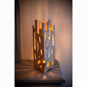 May include: A wooden lamp with a geometric design. The lamp is lit and casts a warm glow.