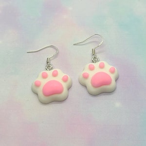 Peut inclure: Une paire de boucles d'oreilles pendantes argentées avec des breloques en forme de patte de chat rose et blanche.