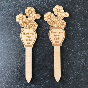 May include: Two wooden plant markers featuring a vase and flower design. The markers are personalised with the text "Thank you from Fergus XXX" and "Thank you from Seth XXX".
