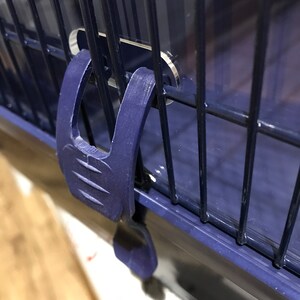 Op de afbeelding: Close-up van een blauwe plastic sluiting op een blauwe metalen kooi. De sluiting heeft een getextureerd oppervlak en is ontworpen om de kooi te beveiligen.