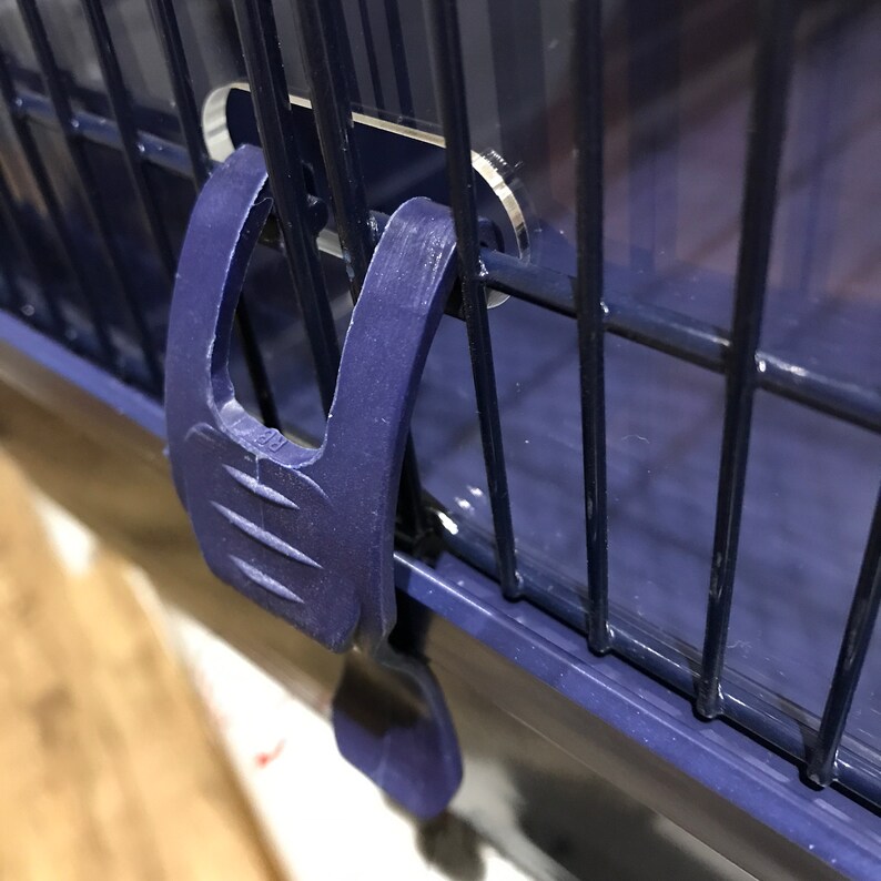 Op de afbeelding: Close-up van een blauwe plastic sluiting op een blauwe metalen kooi. De sluiting heeft een getextureerd oppervlak en is ontworpen om de kooi te beveiligen.