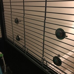 May include: Close-up of a metal cage with four silver clips attached to the side. The clips are used to secure a clear plastic panel to the cage.