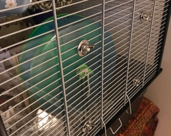 May include: A black metal hamster cage with a clear plastic wheel and a blue and white fabric hammock. The cage has four silver clips on the side.