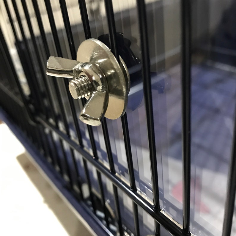 Op de afbeelding: Close-up van een zilveren metalen vergrendeling met een vleugelmoer op een zwarte metalen kooi.