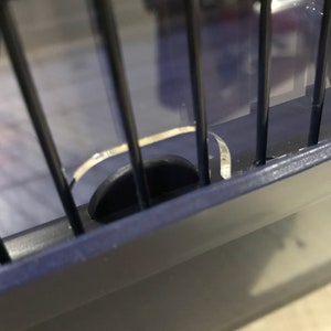 Op de afbeelding: Close-up van een blauwe metalen kooi met een zwart plastic slot. Het slot is gedeeltelijk open, waardoor de binnenkant van de kooi zichtbaar is.