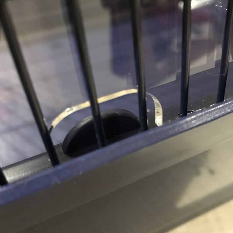 Op de afbeelding: Close-up van een blauwe metalen kooi met een zwart plastic slot. Het slot is gedeeltelijk open, waardoor de binnenkant van de kooi zichtbaar is.