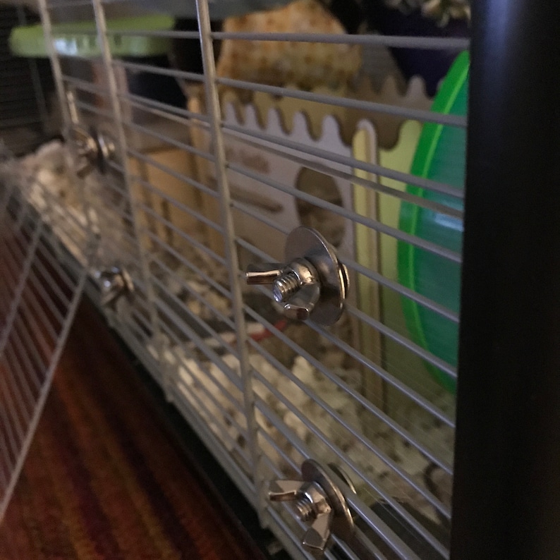 May include: Close-up of a silver metal cage clip with a round base and a small knob. The clip is attached to a wire cage.