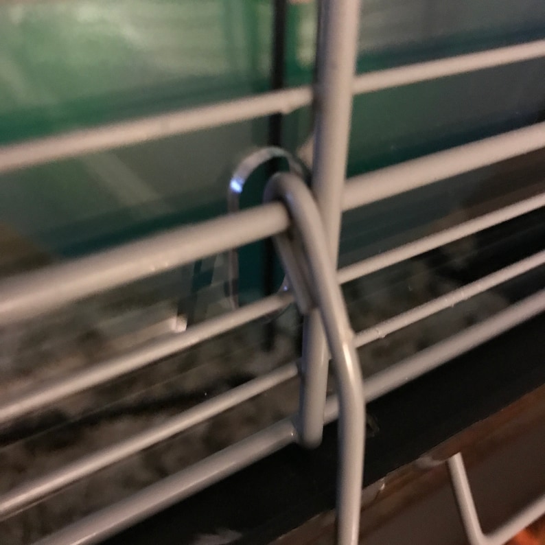 May include: Close-up of a silver metal cage door with a latch. The latch is bent at a 90-degree angle and is secured to the cage door.