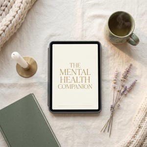 May include: A tablet with the text "THE MENTAL HEALTH COMPANION" is surrounded by a green book, a candle in a gold holder, a mug of tea, and lavender sprigs. A cream-colored knitted blanket is in the background.