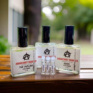 May include: Three glass bottles of cologne with black caps and labels. The labels feature an anarchy symbol and the text "Anarchist Soap Co.". The bottles are labelled "The Outlaw Cologne", "Eden Cologne", and "Vicious Cologne".