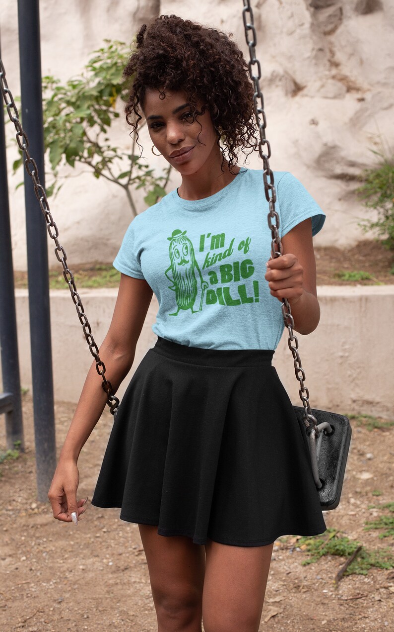 May include: A light blue t-shirt with a green cartoon pickle wearing a hat and holding a cane. The text on the shirt reads "I'm kind of a BIG dill!"