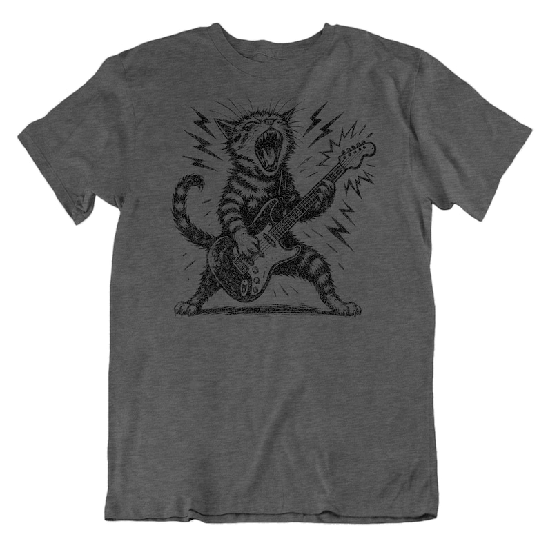 May include: Dark gray t-shirt featuring a black and white illustration of a cat playing an electric guitar. The cat is depicted with its mouth open, surrounded by lightning bolts, creating a rock and roll theme.