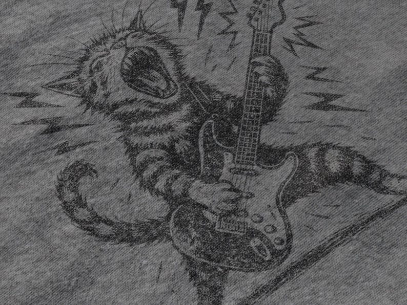 May include: A grayscale illustration of a cat playing an electric guitar. The cat is depicted with an open mouth, as if roaring, and is surrounded by lightning bolt graphics. The guitar is a classic six-string model.