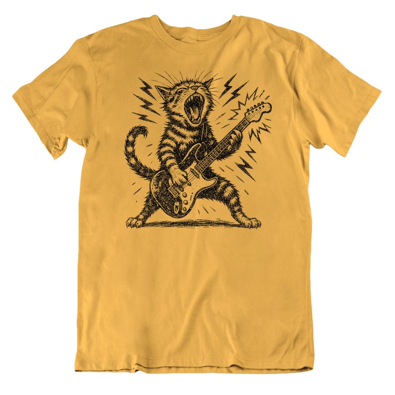 May include: Mustard yellow t-shirt featuring a black and white illustration of a cat playing an electric guitar. The cat is roaring with lightning bolts in the background. The shirt is made of a soft, comfortable material.